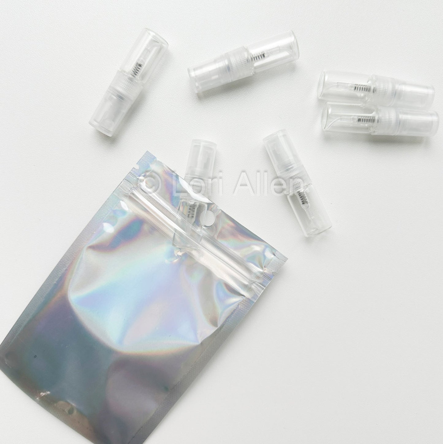 Set of clear plastic vials with a holographic pouch on a white background