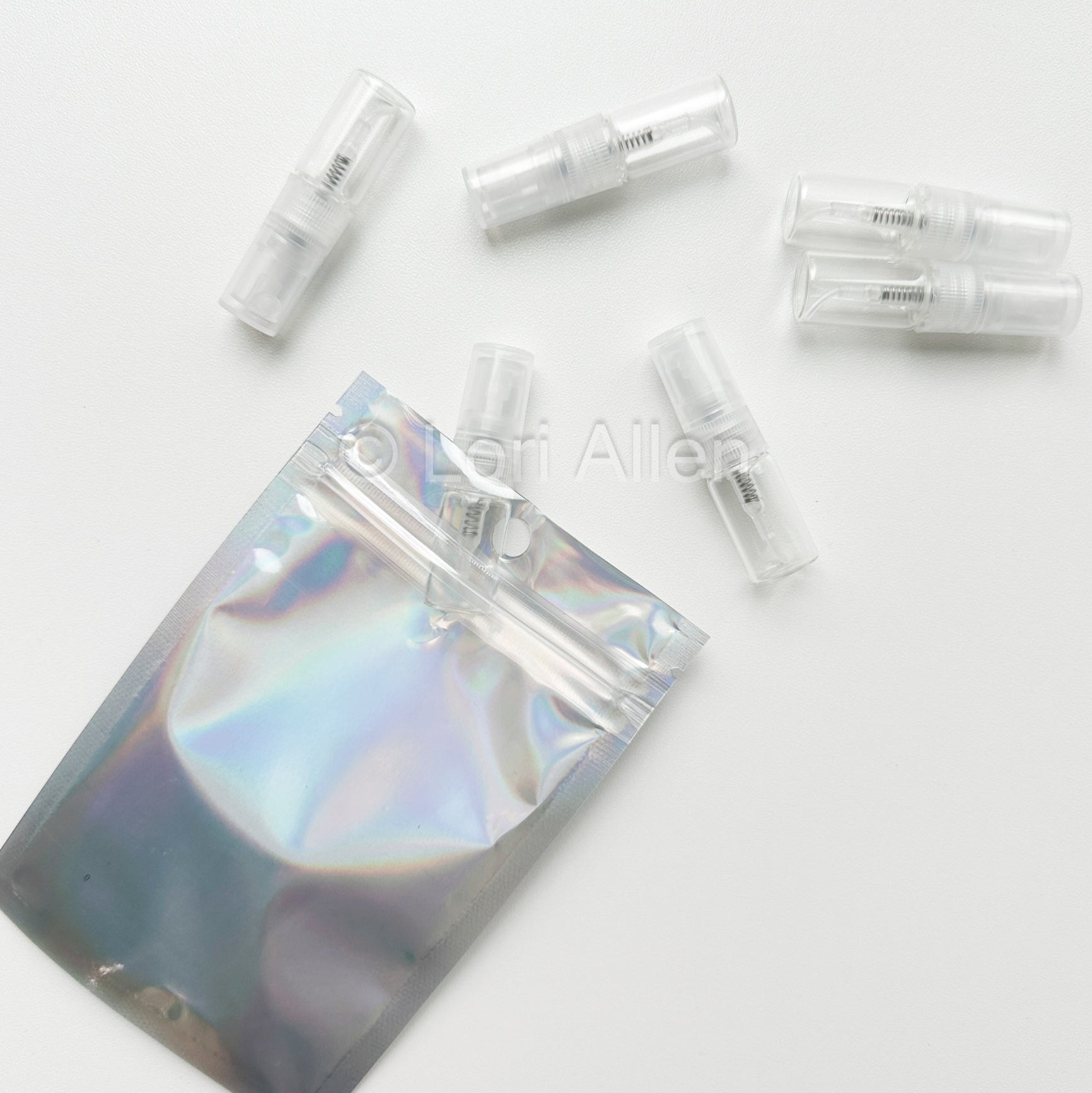 Set of clear plastic vials with a holographic pouch on a white background